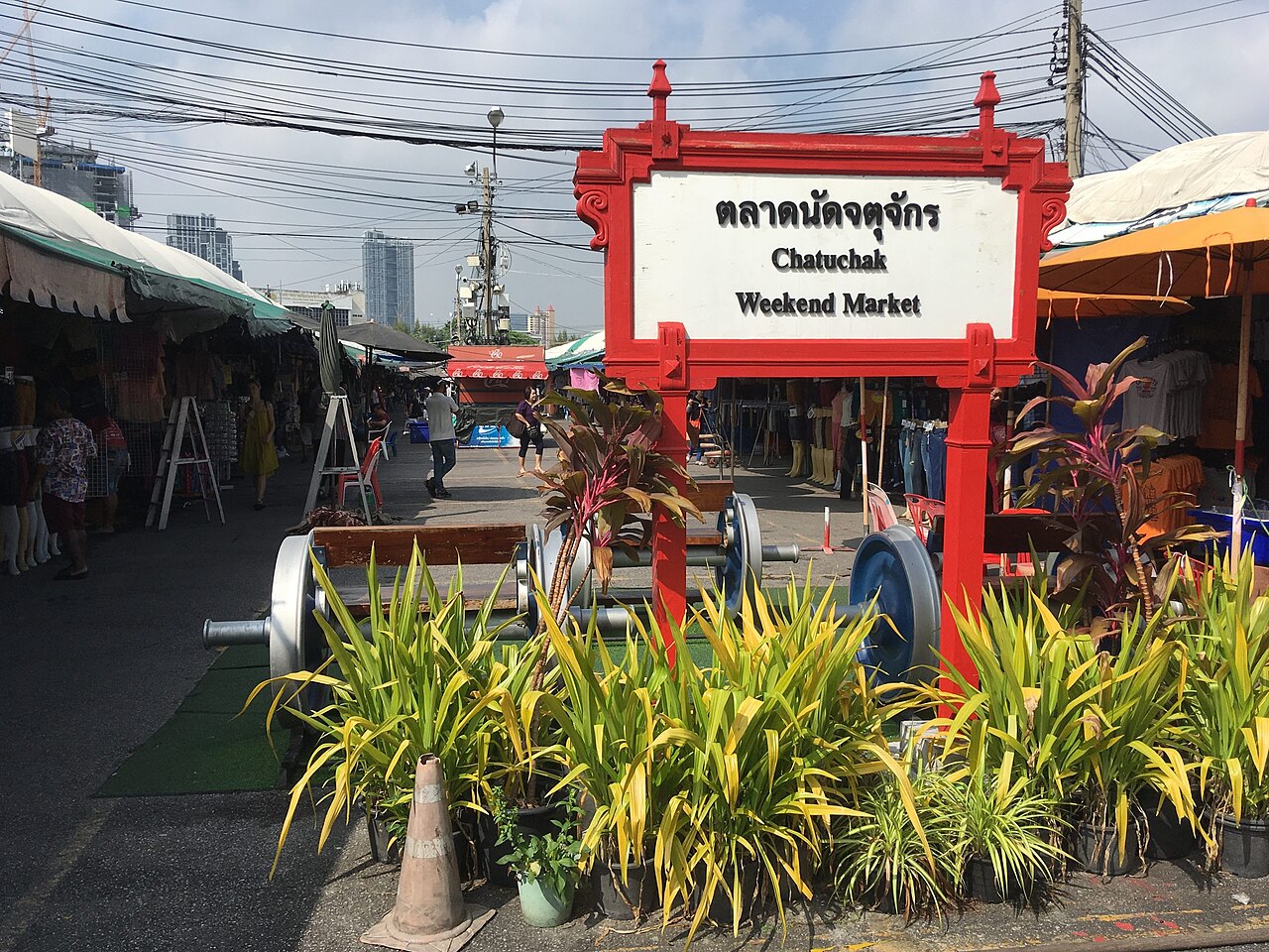 ตลาดนัดจตุจักร กรุงเทพฯ — ป้ายตลาดนัดจตุจักรสีแดงหน้าซอยร้านค้า ท้องฟ้าโปร่ง