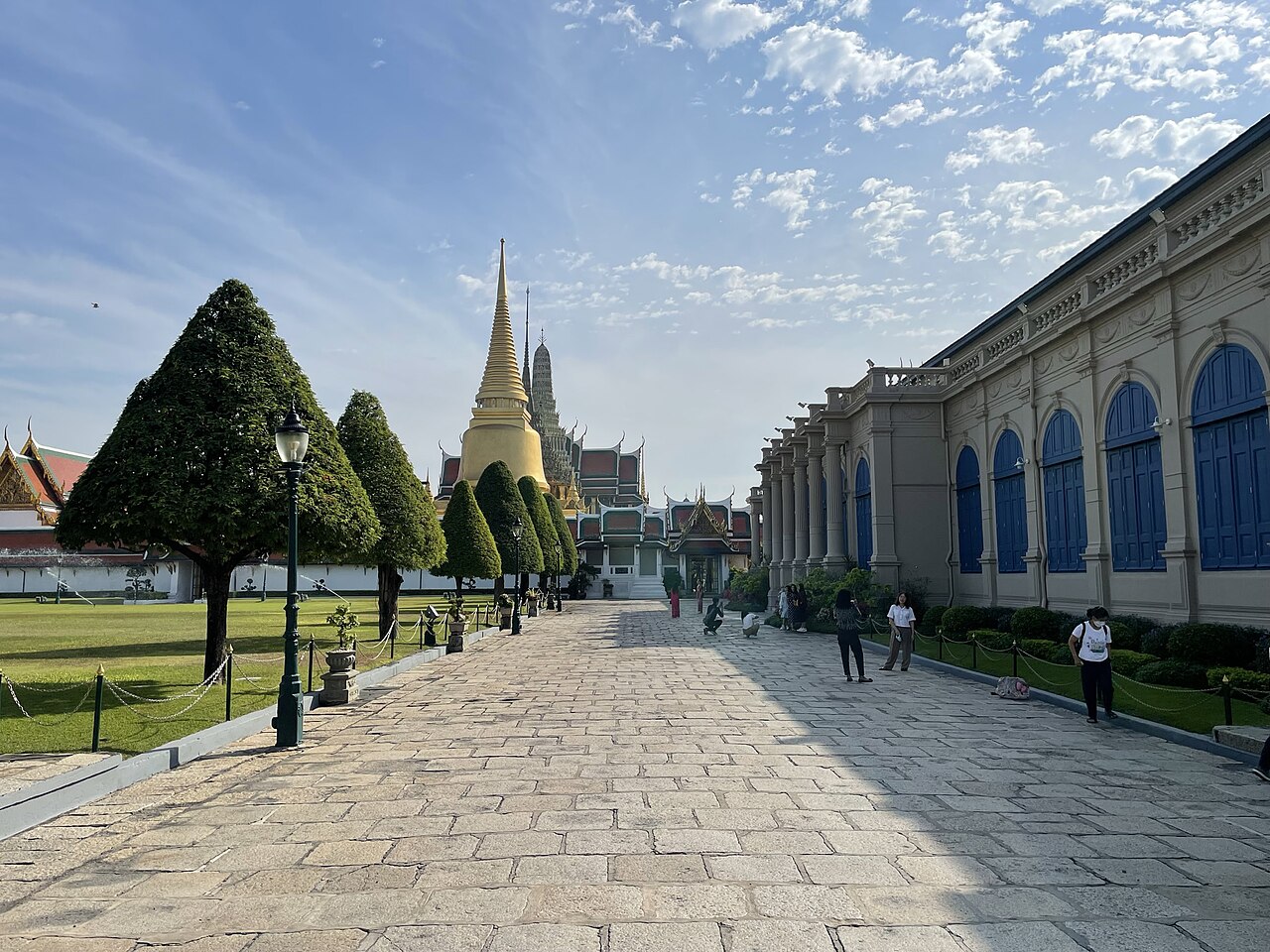 ทางเดินหินภายในพระบรมมหาราชวังยามเช้า มองเห็นพระศรีรัตนเจดีย์สีทองอยู่ปลายทาง คนยังบางตา