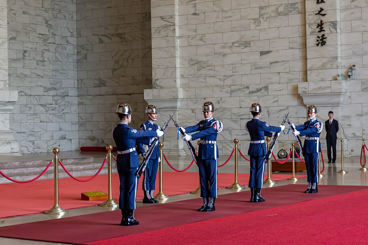 The changing of the honour guard in the upper hall of the Chiang Kai-shek Memorial Hall — five soldiers in blue uniforms with rifles drilling on a red carpet