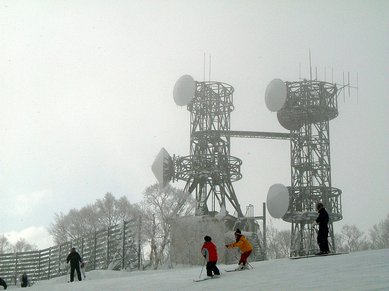 Skiers on a run at Sapporo Teine with frost-coated radio towers on the summit behind