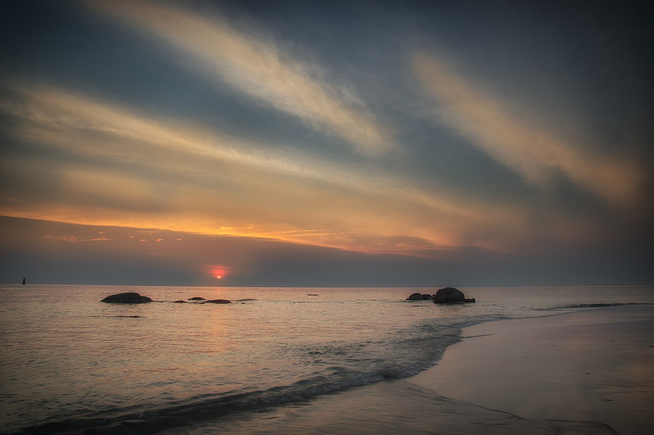 ชายหาดหัวหินยามเช้าในฤดูเย็นและแห้ง ทะเลสงบ มีก้อนหินริมหาดและแสงอ่อนๆ