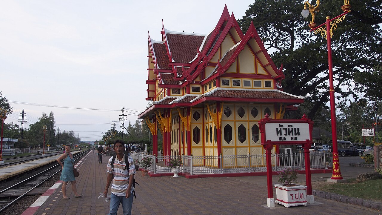 สถานีรถไฟหัวหิน — อาคารพลับพลาสีครีม-แดงสไตล์วิกตอเรียนผสมไทย พร้อมป้ายชื่อสถานีหัวหินและชานชาลาริมราง