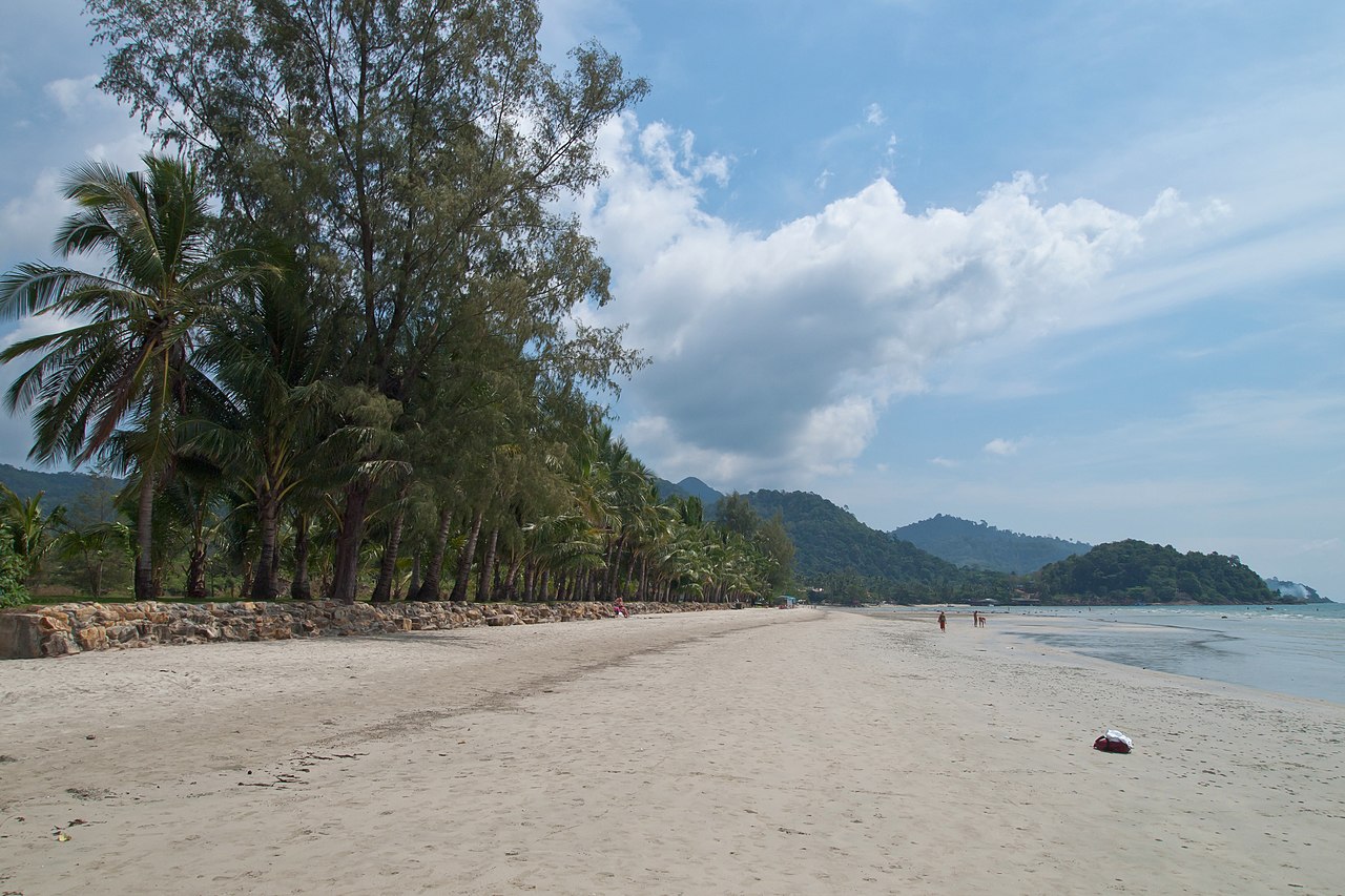 หาดคลองพร้าว เกาะช้าง — หาดทรายยาวเงียบ แถวต้นมะพร้าวและสนทะเล มีภูเขาเขียวเป็นฉากหลัง คนน้อย