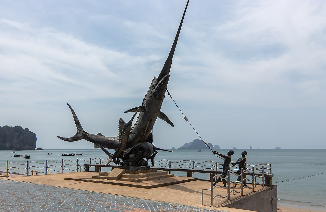 Ao Nang Krabi — a seafront promenade with a sailfish monument, looking out over longtail boats and limestone islands in the sea