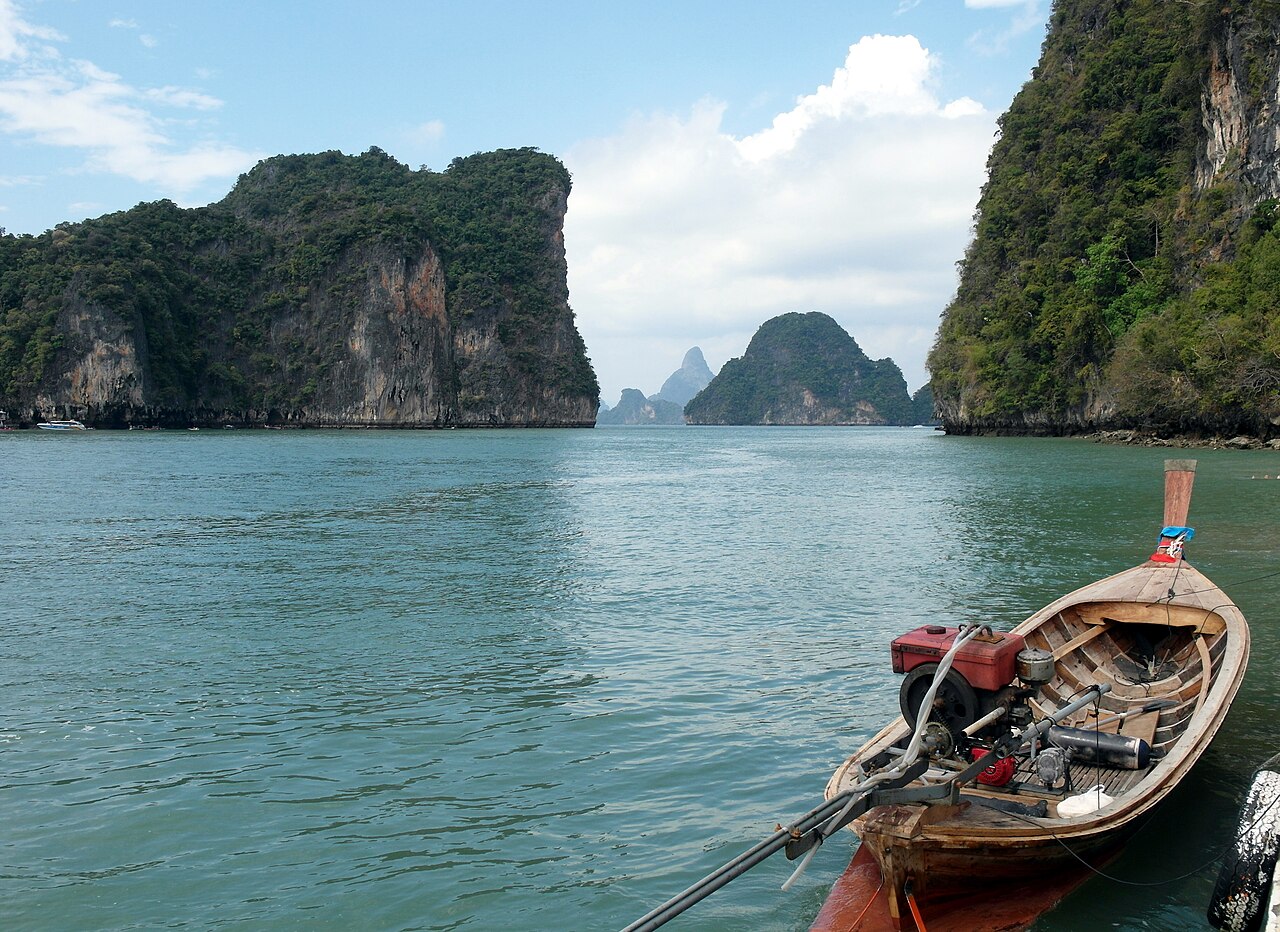 Hong Islands Krabi — a longtail boat floating in a green lagoon enclosed by tall limestone cliffs on both sides