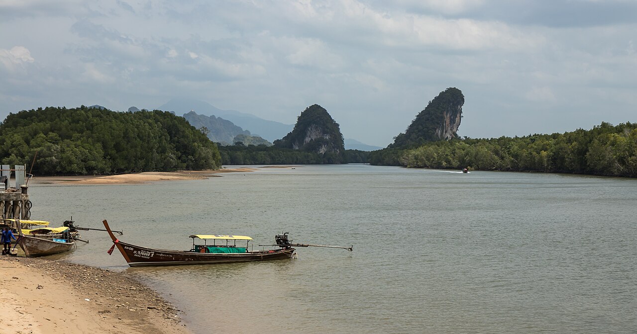Khao Khanab Nam Krabi — twin limestone peaks flanking the Krabi River with longtail boats moored at the bank and mangroves on both sides