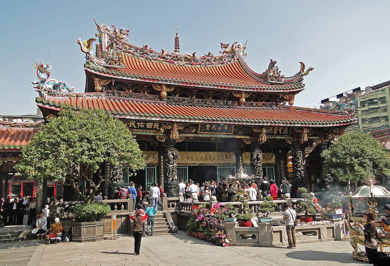 The main hall of Longshan Temple, Taipei, with carved stone columns and incense burners, worshippers gathered in the courtyard