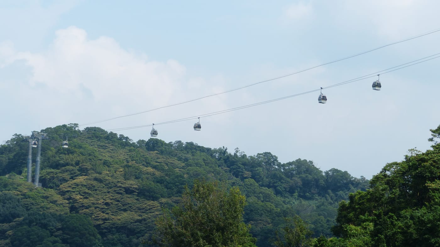 A line of Maokong Gondola cabins strung along the cable across green forested hills in Taipei