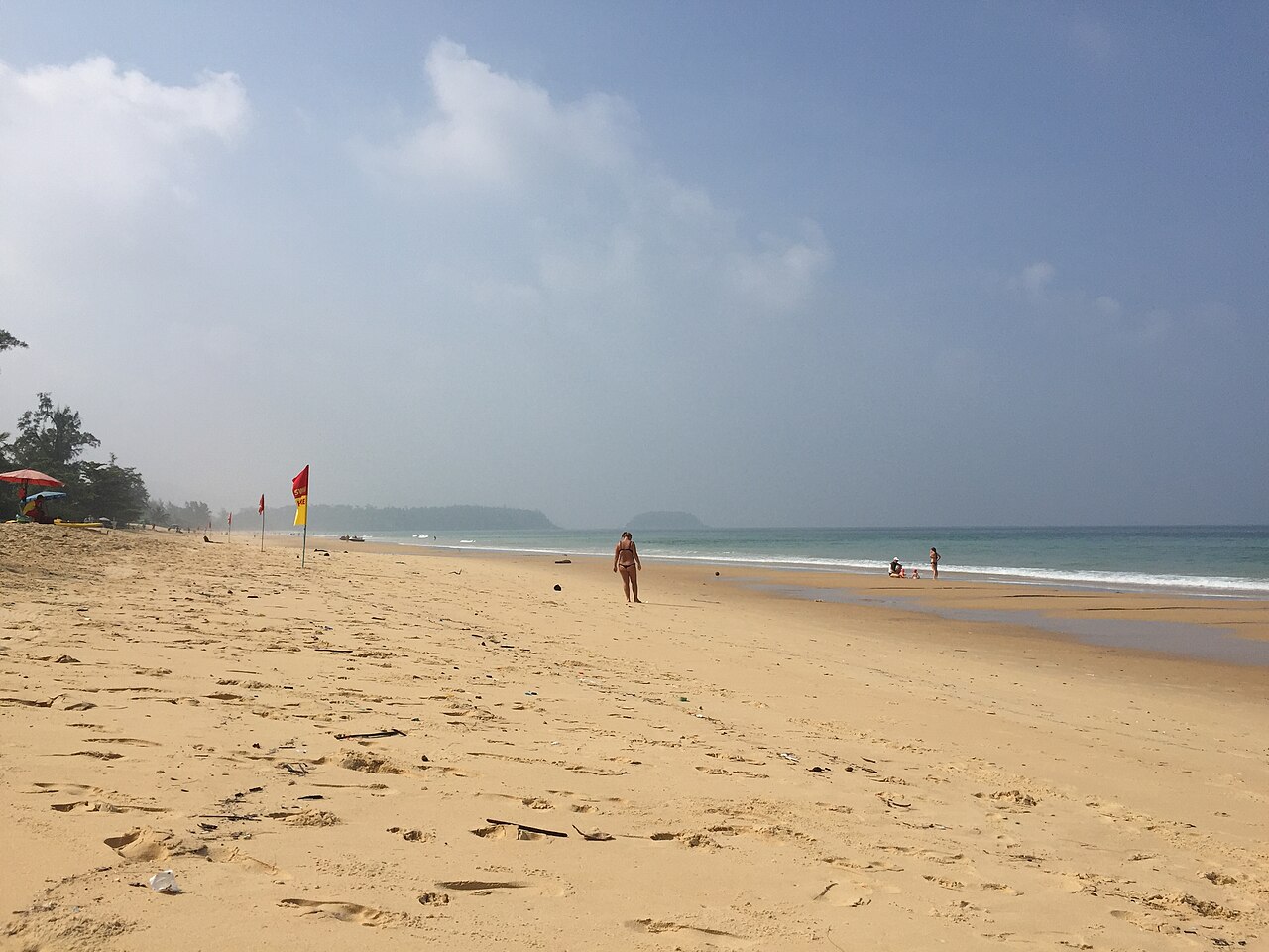 Karon Beach, Phuket — a long wide open white-sand beach with a red warning flag planted in the sand and clear blue sky