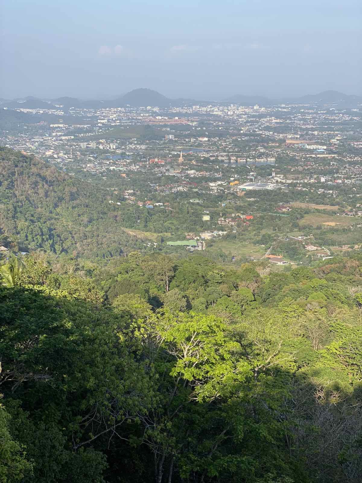 Khao Rang Phuket — looking down from the hill over Phuket Town spread across the plain, with green forest in front and hills and sea in the distance