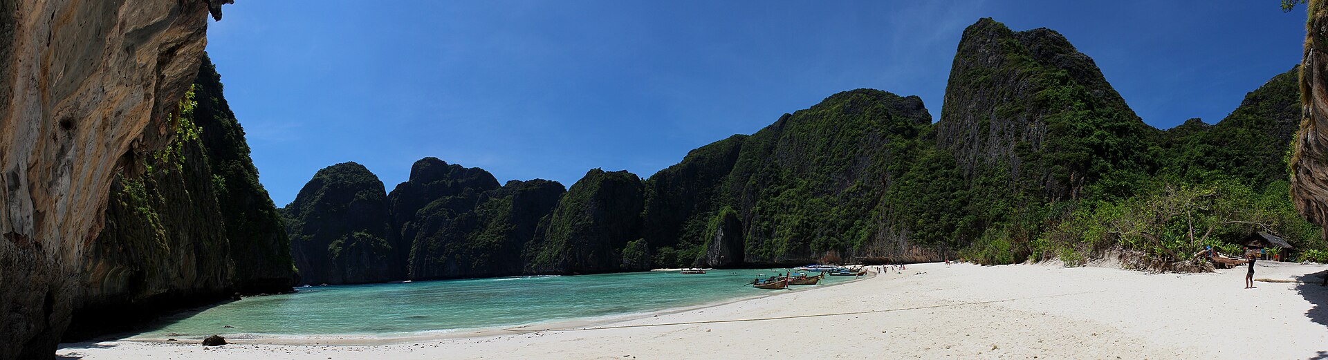 อ่าวมาหยา (Maya Bay) เกาะพีพีเล กระบี่ — หาดทรายขาวโค้งล้อมด้วยหน้าผาหินปูนสูงชัน น้ำทะเลสีฟ้าเขียวใส และเรือหางยาวจอดริมหาด