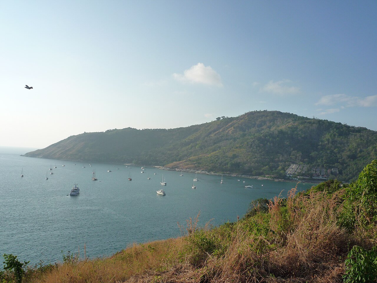 Black Rock viewpoint above Nai Harn Phuket — a panorama of the southern bay with the white-sand arc of Nai Harn beach and the deep-blue Andaman Sea from above