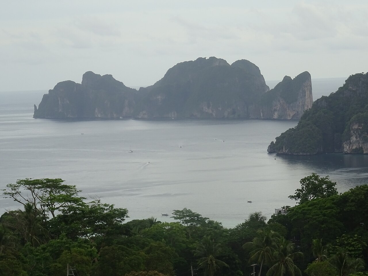 วิวหมู่เกาะพีพีจากมุมสูง — เกาะพีพีเลและพีพีดอนกลางทะเลอันดามัน หน้าผาหินปูนเขียวขจี ทะเลกว้างสีฟ้าเทา เรือเล็กแล่นระหว่างเกาะ