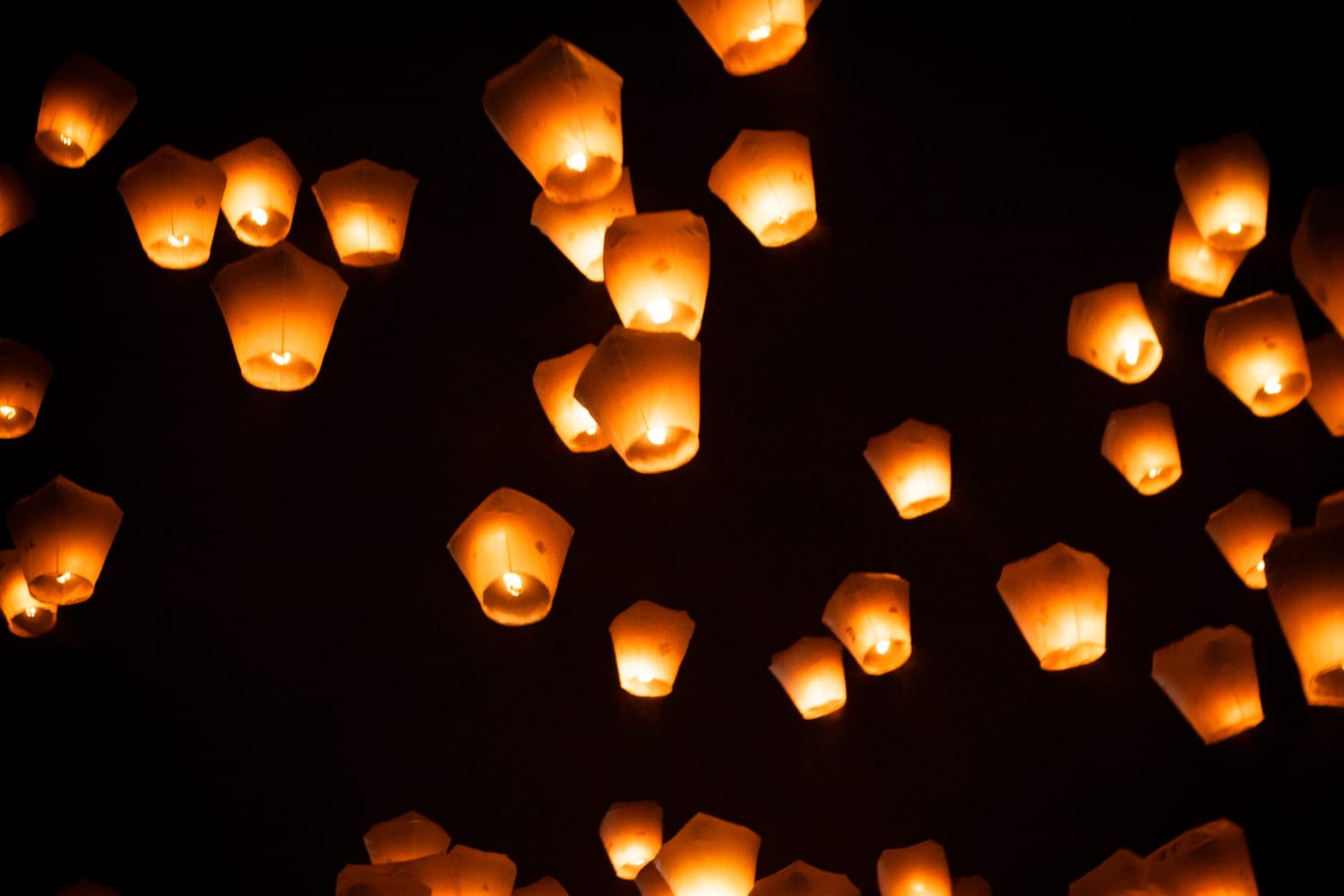 Dozens of paper sky lanterns rising together into a dark sky at the Pingxi Sky Lantern Festival, each glowing with a flame inside