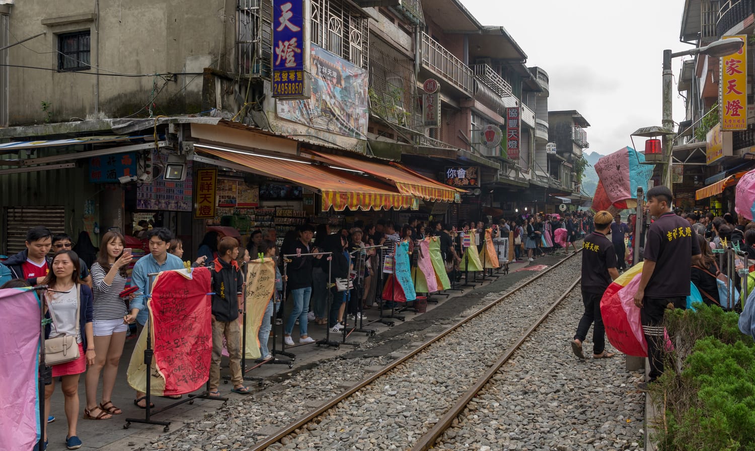 Tourists holding colourful sky lanterns beside the railway tracks on Shifen Old Street