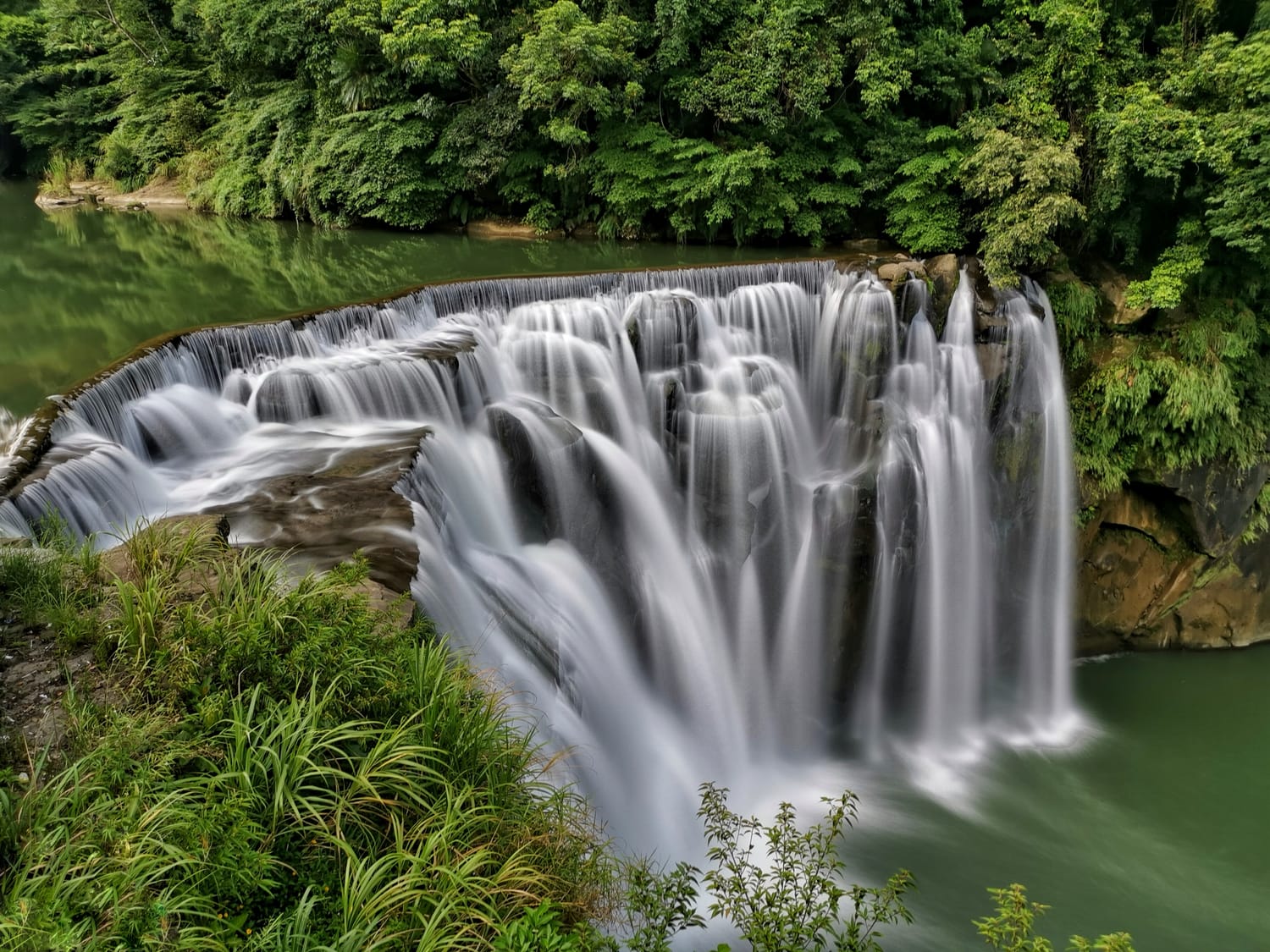 Shifen Waterfall, a wide curtain of water flowing into an emerald pool surrounded by forest