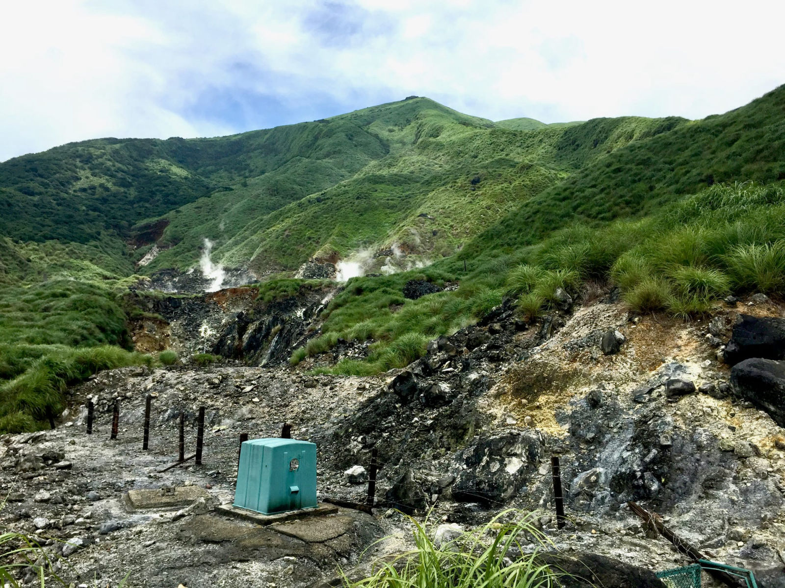 A sulphur geothermal area in Yangmingshan National Park, yellow rock with steam rising along a green hillside