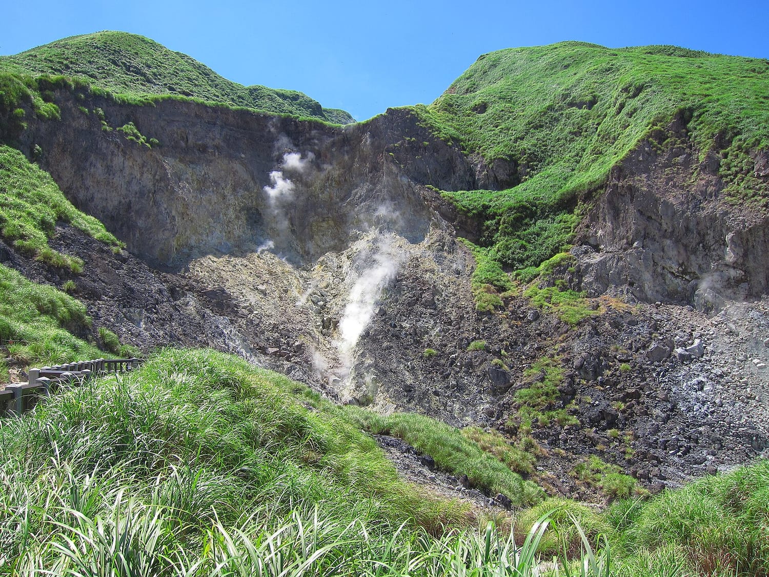 The Xiaoyoukeng sulphur fumarole field in Yangmingshan National Park, steam rising from vents on a yellow rock cliff