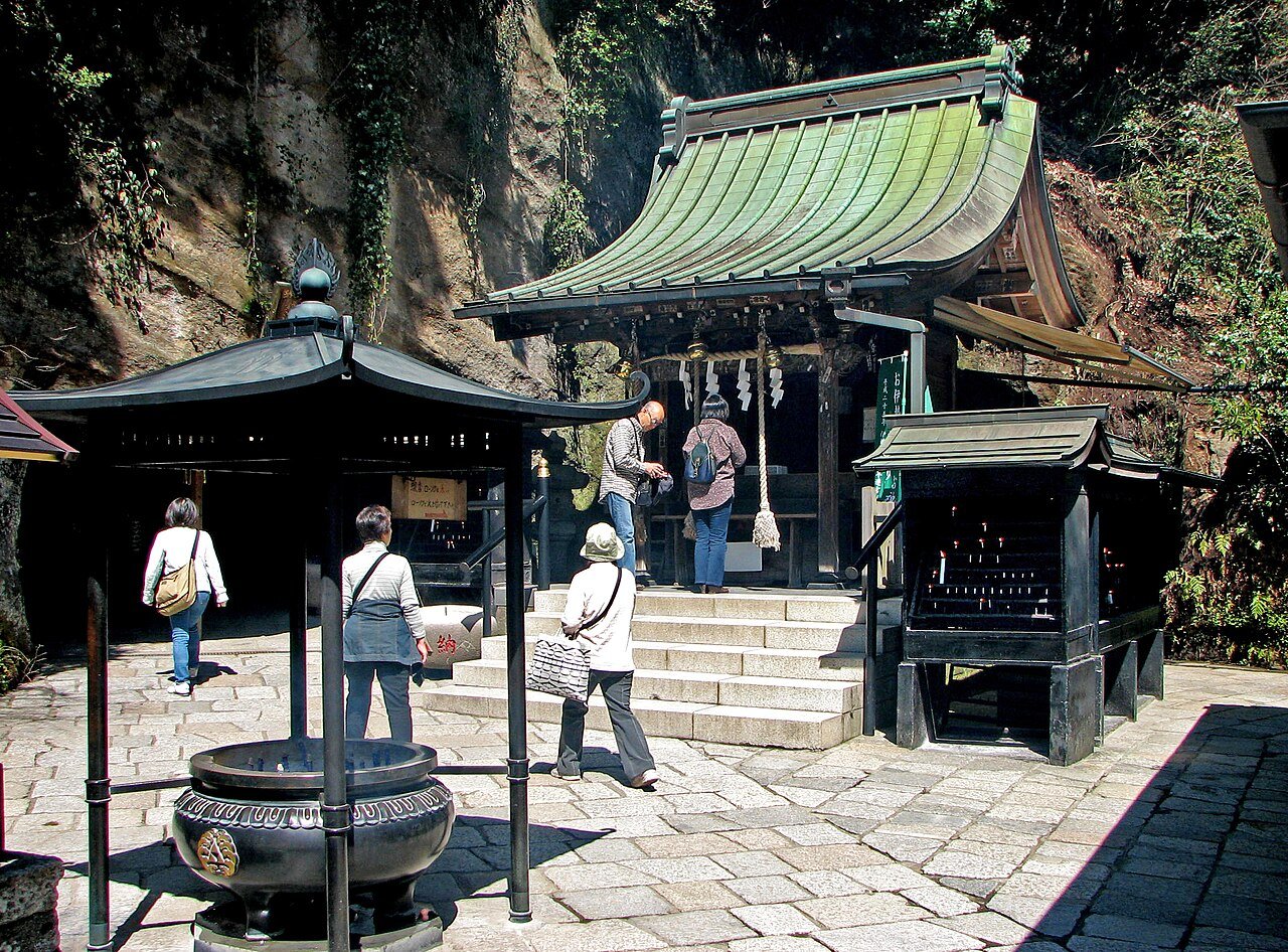 Zeniarai Benten Shrine, Kamakura — a small shrine building set within a rocky cave on a hillside, with worshippers gathered