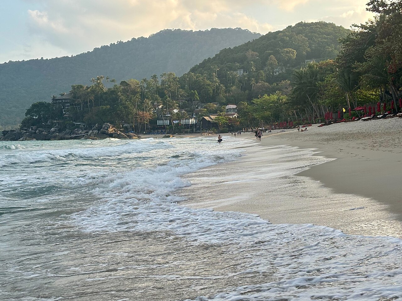 Thong Nai Pan Beach, Koh Phangan — a curved white-sand bay with gentle surf, green mountains behind and warm evening light