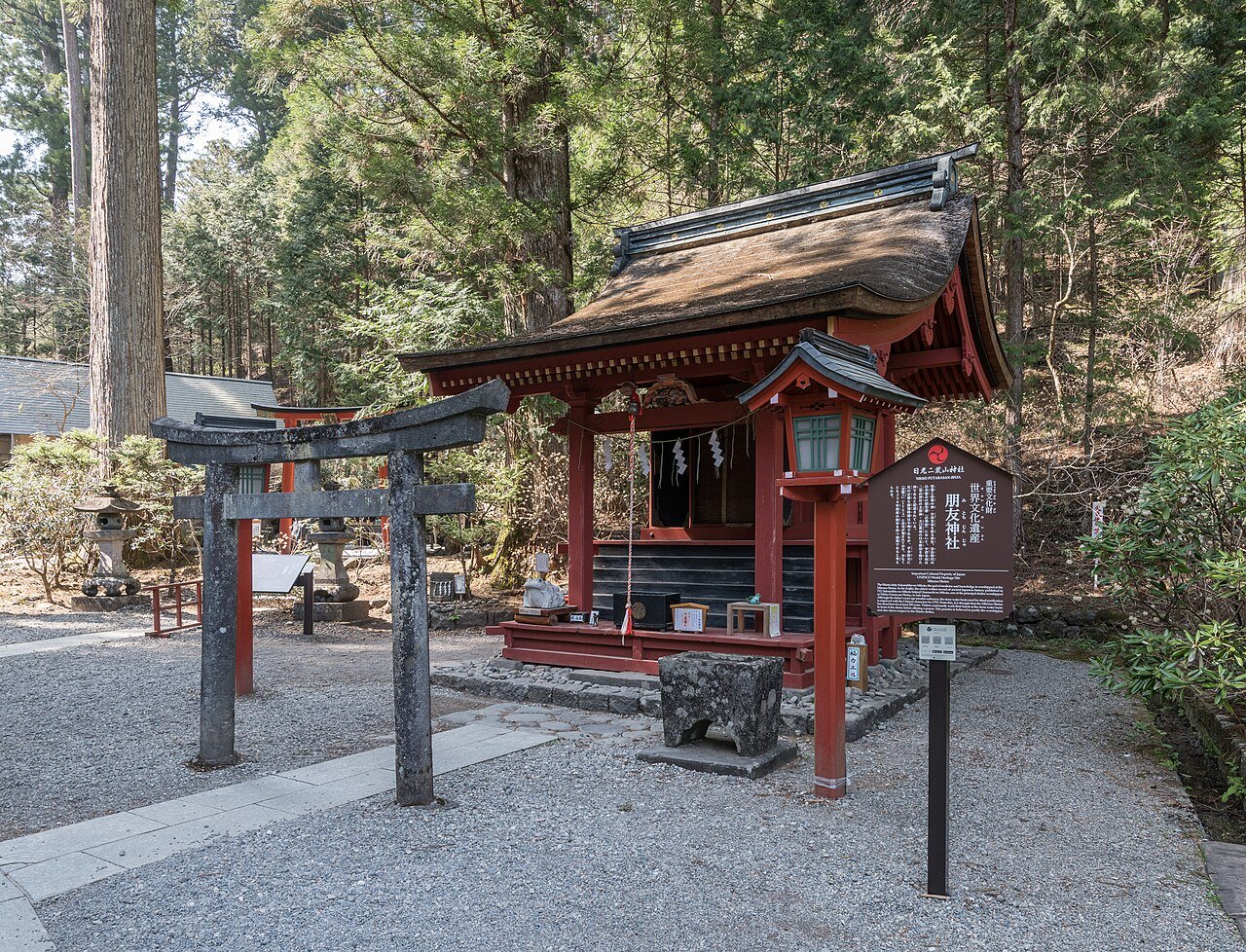 Futarasan Shrine, Nikko — a small vermilion thatched-roof shrine with a stone torii gate, set in cedar forest