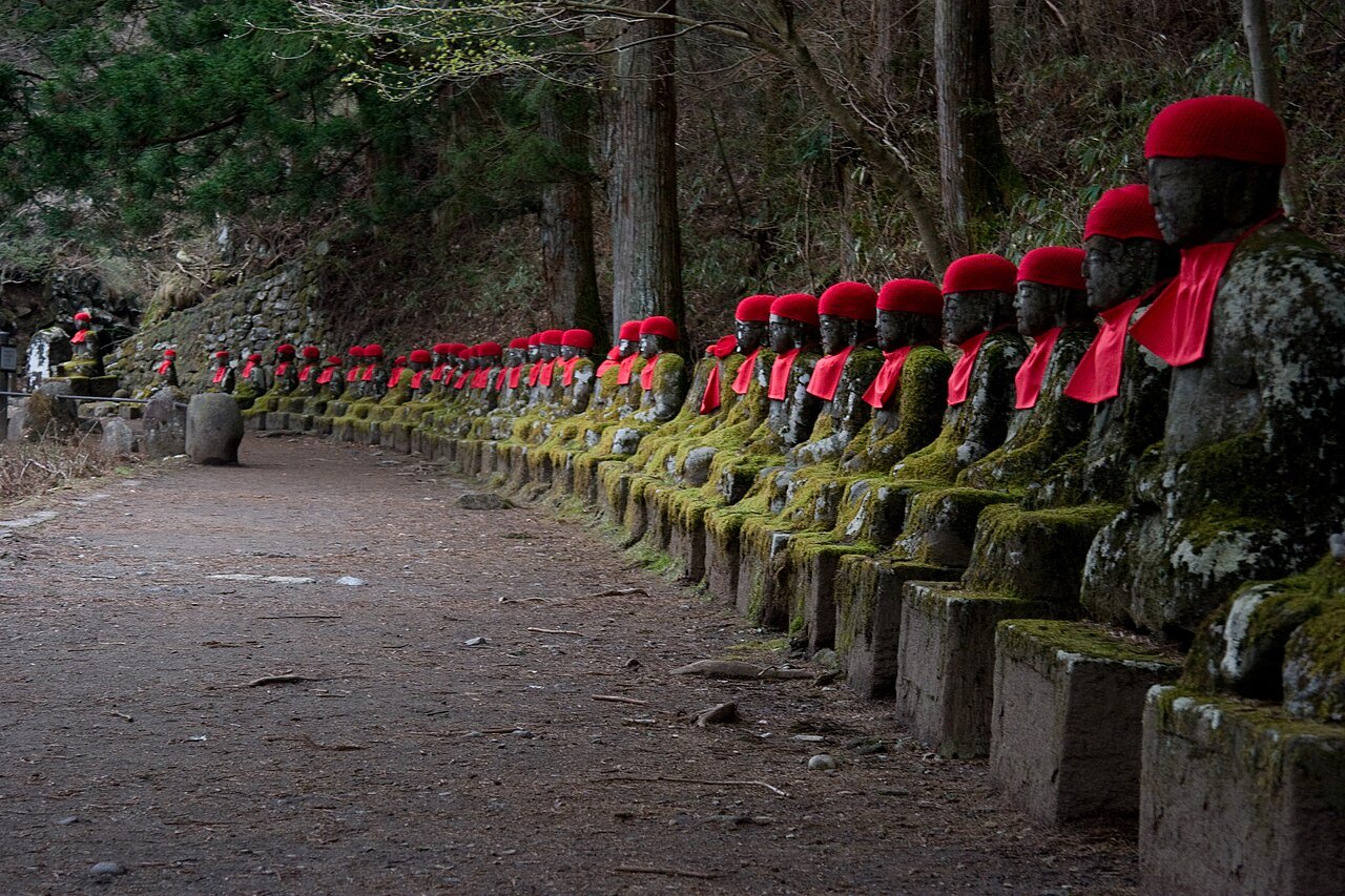 Kanmangafuchi Abyss, Nikko — a long row of stone Jizo statues in red caps and bibs lining a forested riverside gorge