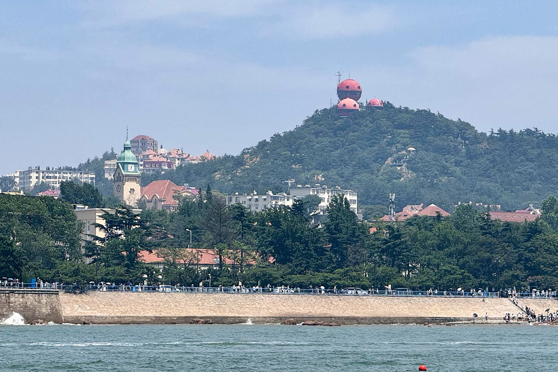 เขาซิ่นห้าว ชิงเต่า — หอชมวิวโดมสีแดงบนยอดเนิน มองลงเห็นหลังคาแดงของเมืองเก่าและอ่าวทะเล