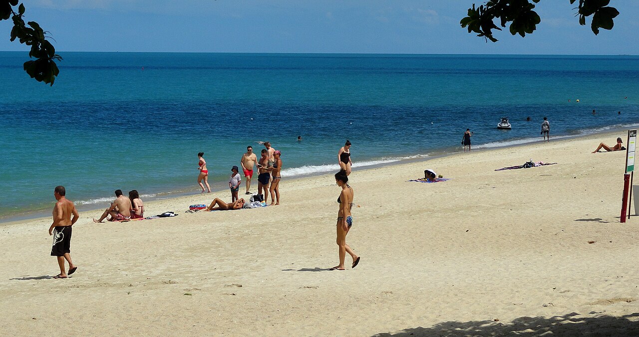 หาดละไม เกาะสมุย — หาดทรายขาวโค้งยาว น้ำทะเลสีฟ้าใส คนนอนอาบแดดและเล่นน้ำแบบสบายๆ