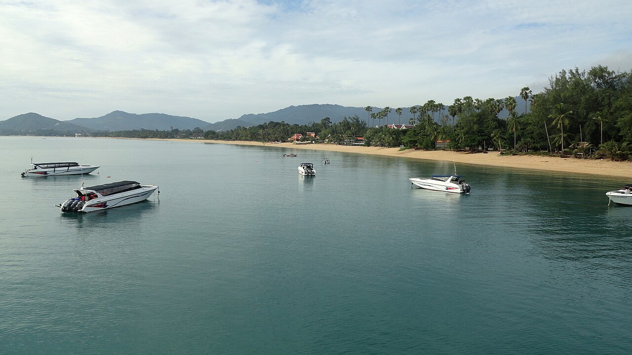 หาดแม่น้ำ เกาะสมุย — หาดยาวเงียบสงบ แนวมะพร้าวริมทราย เรือเร็วจอดลอยลำในอ่าว