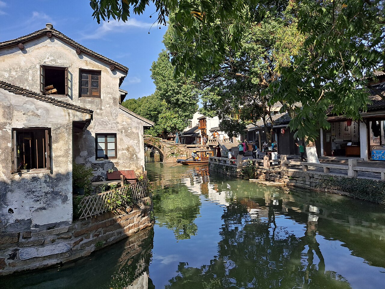Canal in Zhouzhuang, China's No.1 water town — old whitewashed houses by the water, an arched stone bridge and a wooden boat reflected in the green canal