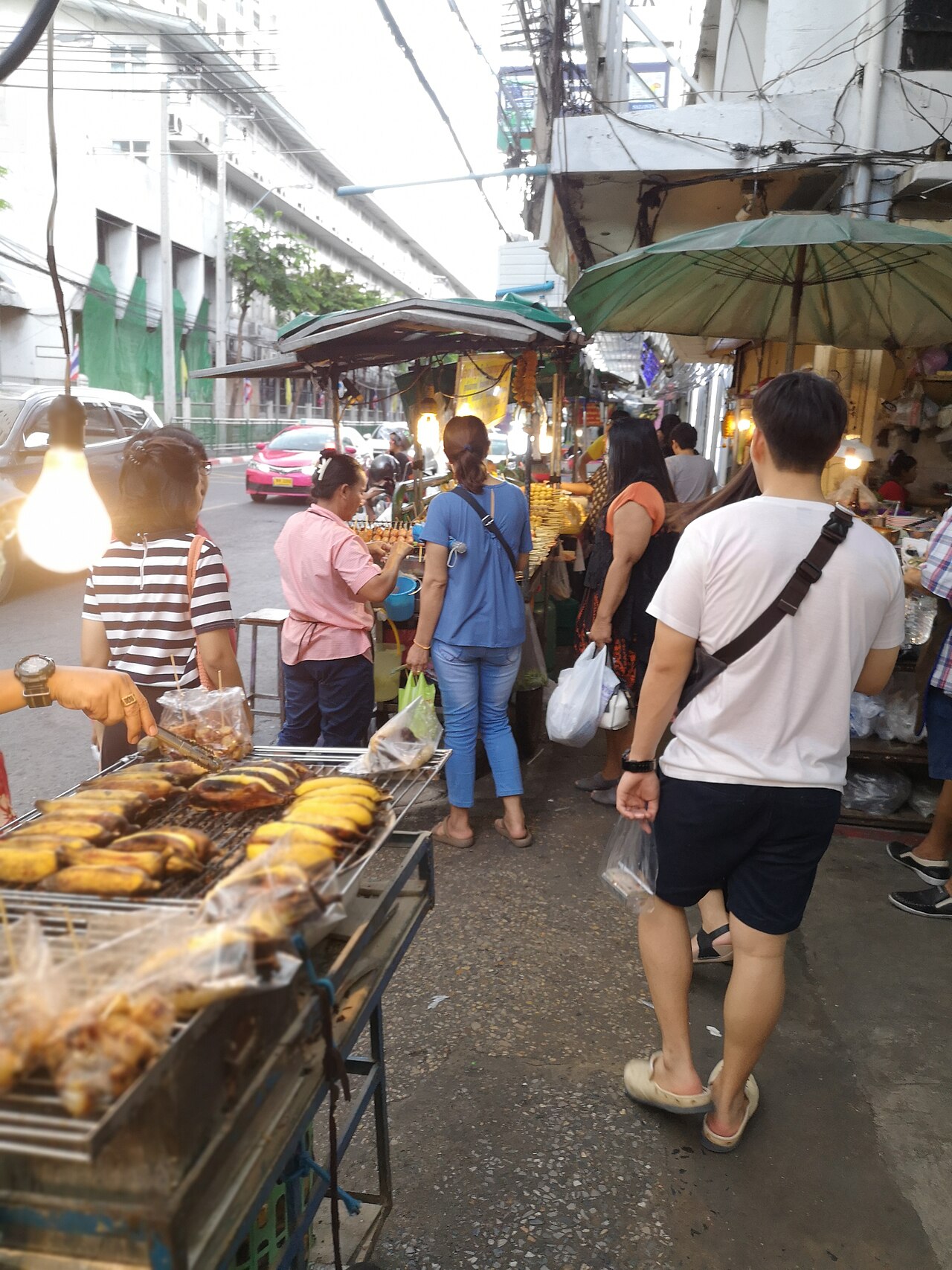 ตรอกตลาดวังหลังฝั่งธนบุรี — แผงกล้วยปิ้งข้าวโพดย่างริมทาง ร่มกันแดดและผู้คนเดินซื้อของกิน