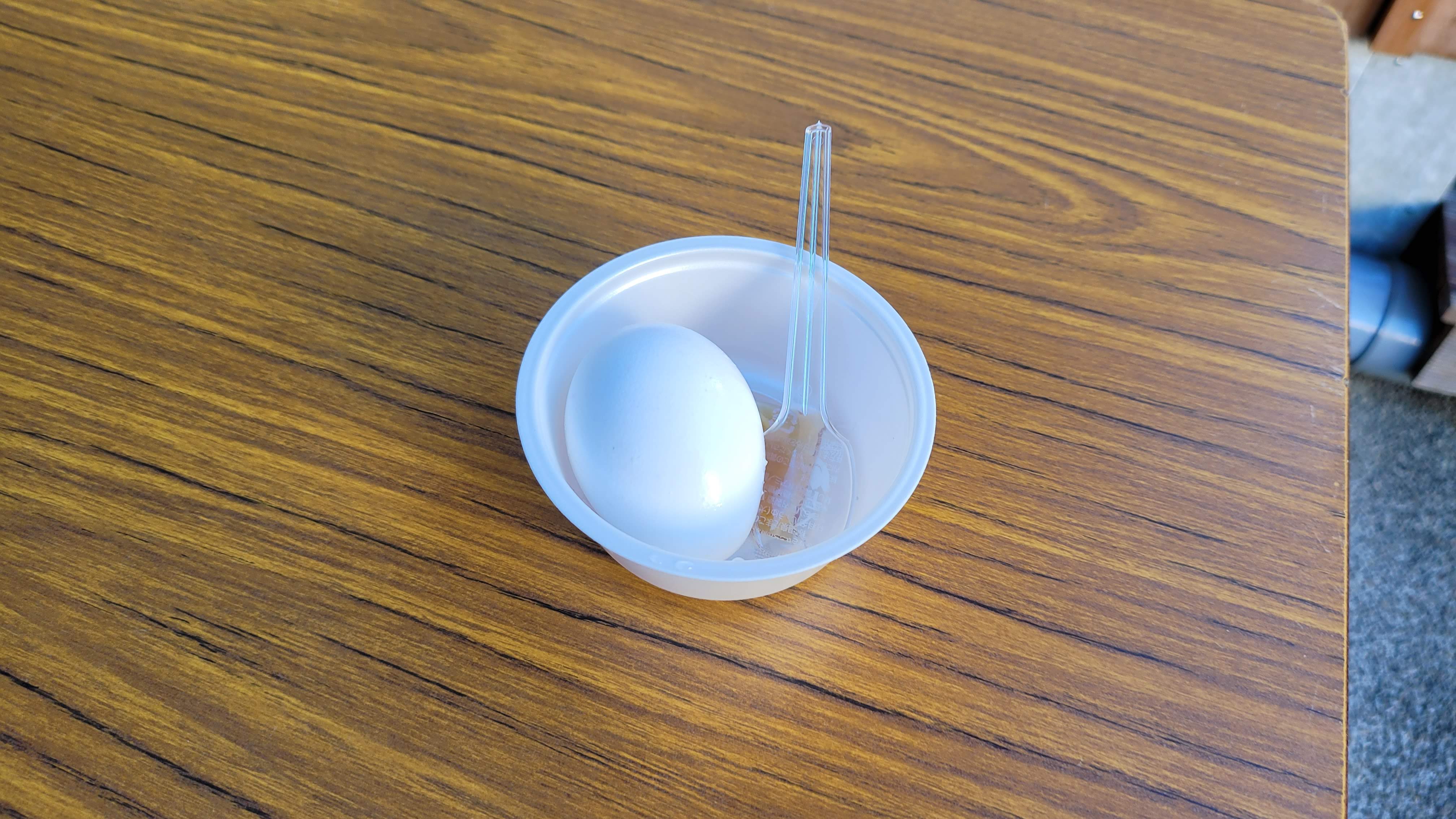 Onsen tamago — a hot-spring-cooked egg served in a small white bowl with a plastic spoon, the egg white set to a soft custard texture