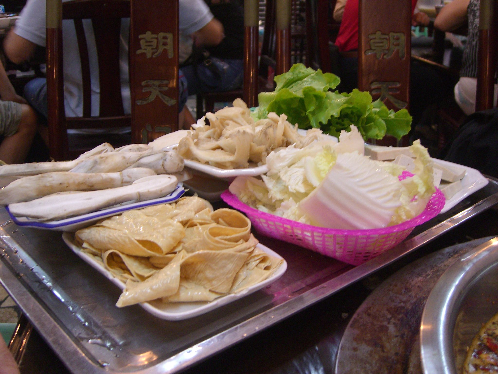 A tray of hotpot vegetables — mushrooms, tofu skin, Chinese cabbage and lettuce on a steel table in a hotpot restaurant