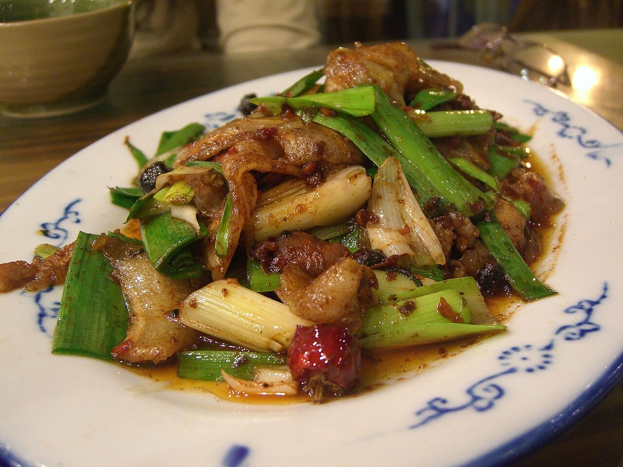 หมูผัดสองครั้ง หมูสามชั้นสไลด์ม้วนผัดกับต้นกระเทียมในน้ำพริกเต้าเจี้ยวเงาวับ บนจานลายน้ำเงิน