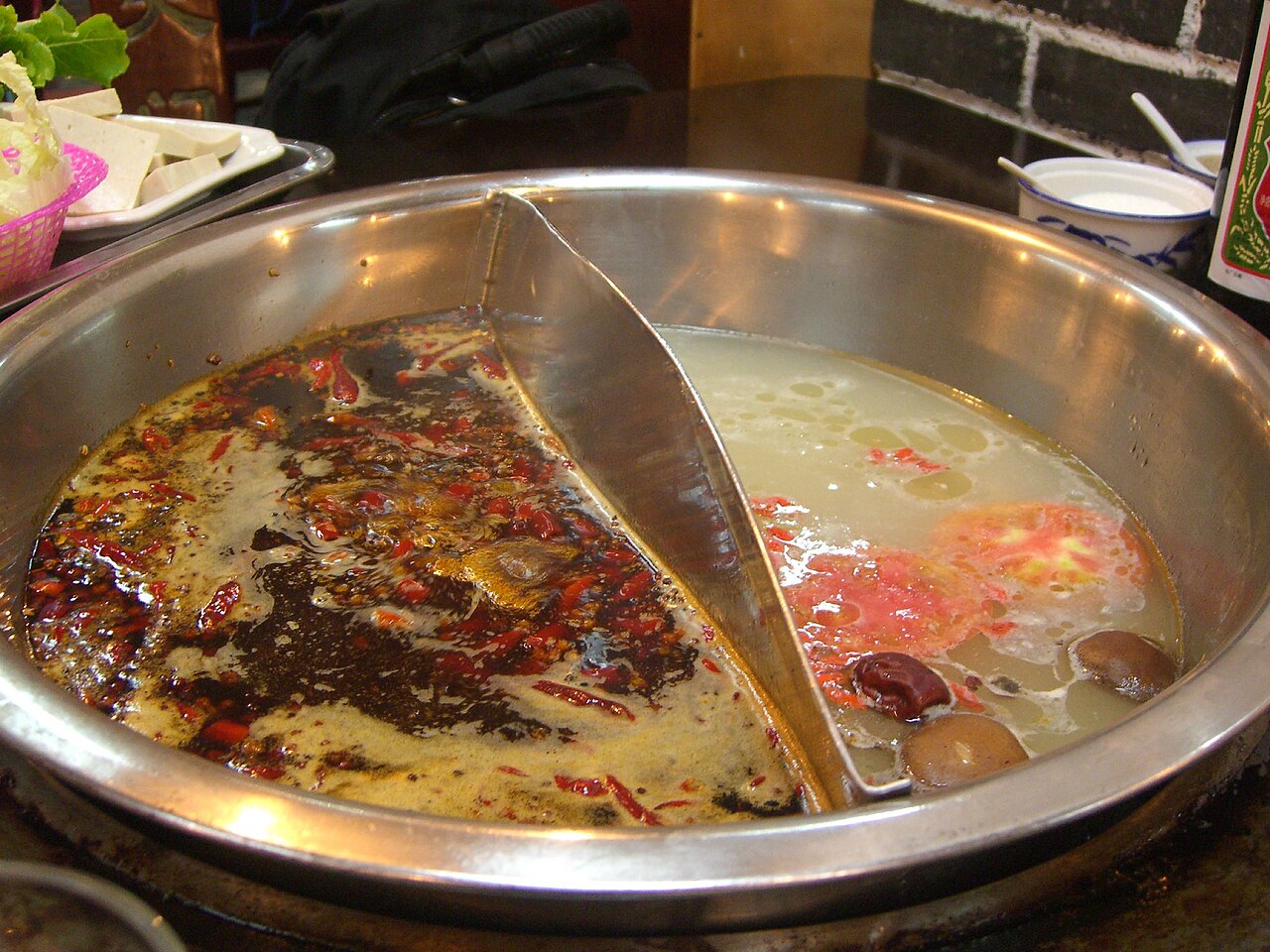 A divided yuanyang hotpot, left side red málà broth with floating chillies and Sichuan peppercorns, right side clear broth