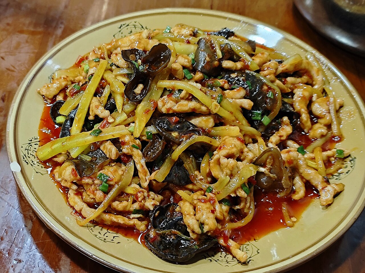 Yuxiang rousi — shredded pork stir-fried with wood-ear mushroom, bamboo shoots and spring onion in a glossy red-orange sauce on a patterned plate
