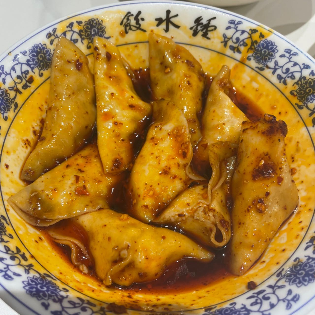 Zhong dumplings — crescent-shaped dumplings in a blue-and-white bowl, coated in red chili oil and sweet soy sauce