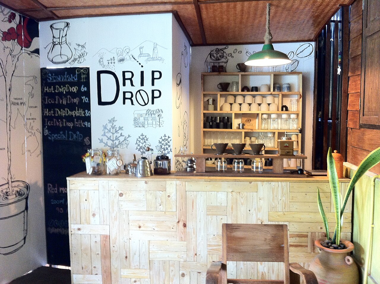 Inside a specialty café in Chiang Mai — a wooden counter, shelves of cups and drip gear, a hand-written menu board and hand-drip brewing equipment
