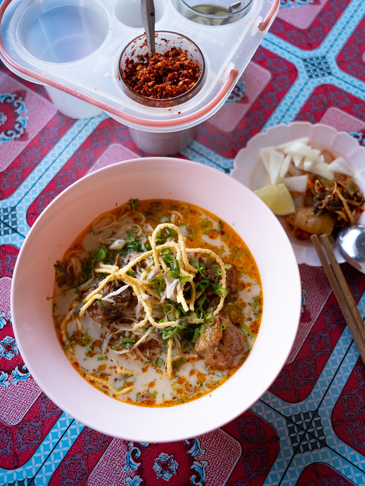 ข้าวซอยหนึ่งชามเสิร์ฟบนโต๊ะลายผ้าพื้นเมือง โรยเส้นทอดกรอบ ตัวอย่างจานเหนือที่ได้ทำในคลาสเต็มวันที่เชียงใหม่