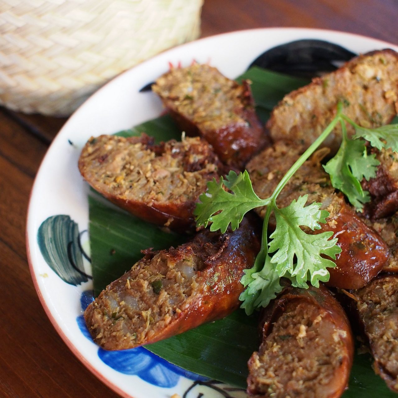 Sai ua — coils of grilled northern Thai herb sausage sliced on a banana leaf, with a basket of sticky rice