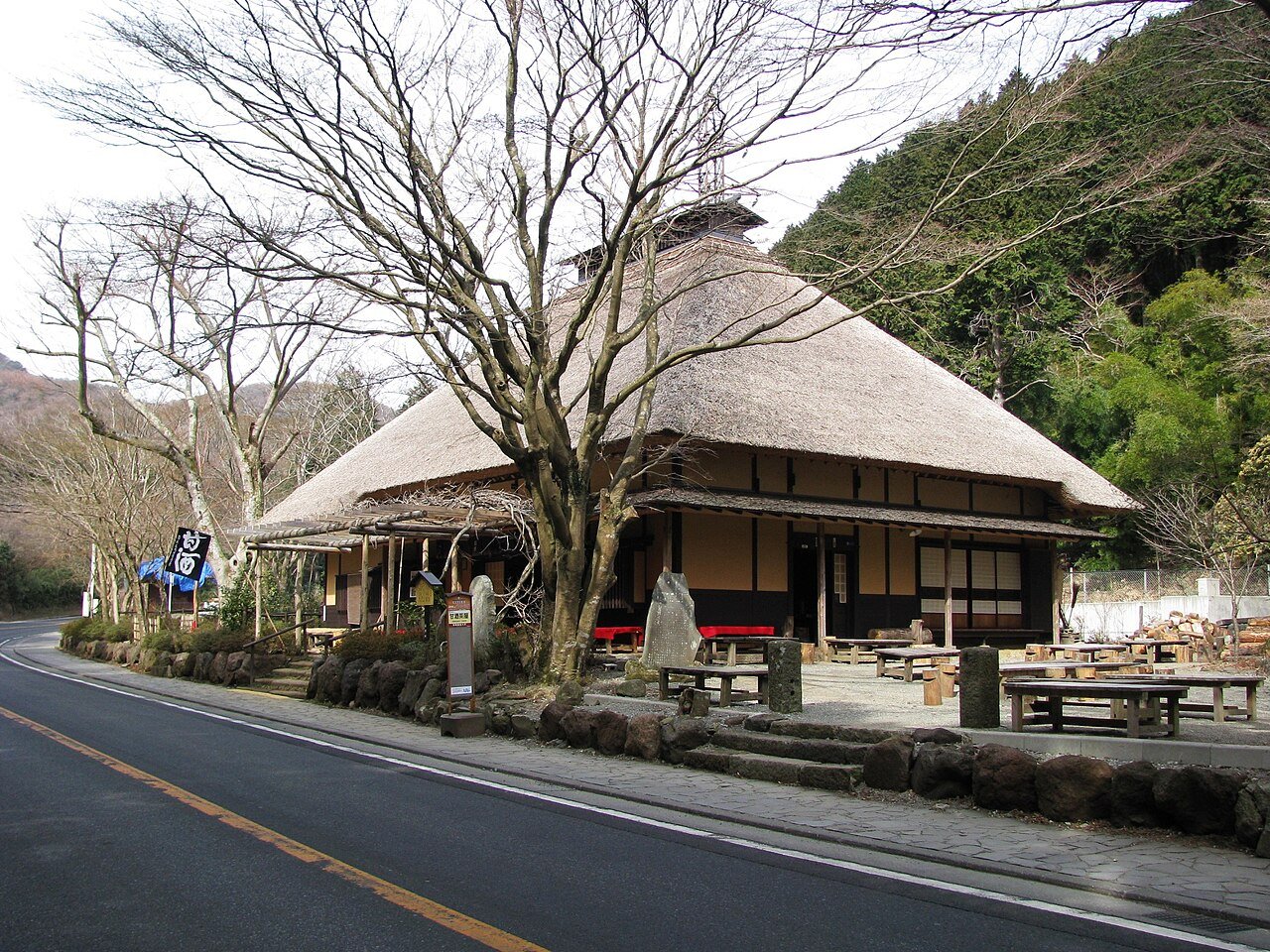 The historic thatched-roof Amazake Chaya teahouse, over 400 years old, on the old Tokaido mountain road in Hakone, Kanagawa, surrounded by trees with wooden benches outside