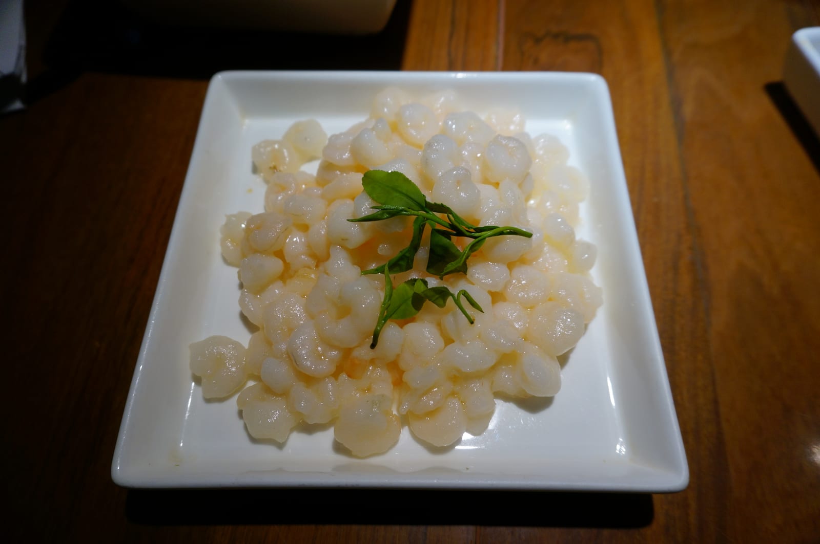 กุ้งหลงจิ่ง กุ้งแม่น้ำตัวเล็กสีขาวผัดสุกวางบนจานเหลี่ยมขาว โรยใบชาเขียวหลงจิ่งสด