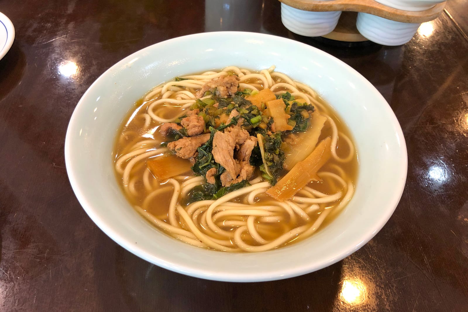 เพี่ยนเอ๋อชวน บะหมี่เส้นในน้ำซุปใสสีน้ำตาล มีหมูสไลซ์ ผักดอง และหน่อไม้ในชามขาว