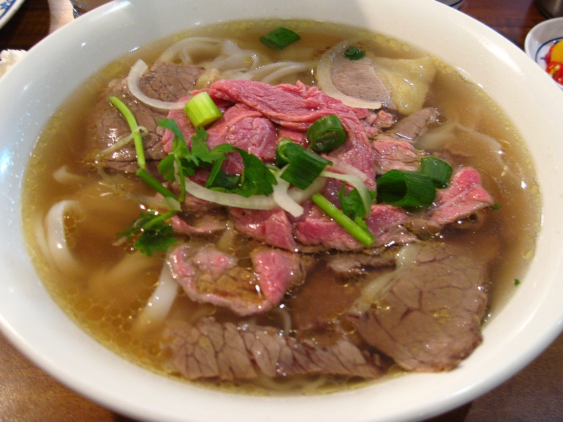 A large bowl of Vietnamese pho with noodles, beef, and fresh herbs