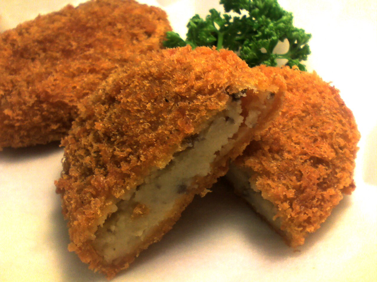 Japanese korokke croquette split open showing a pale potato and meat filling inside a dark-golden panko breadcrumb crust, garnished with parsley