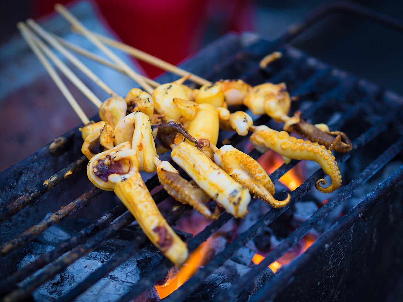 Skewers of grilled squid charring over an open charcoal flame — the kind of street-style seafood grill found at beachside stalls and evening markets on Koh Chang