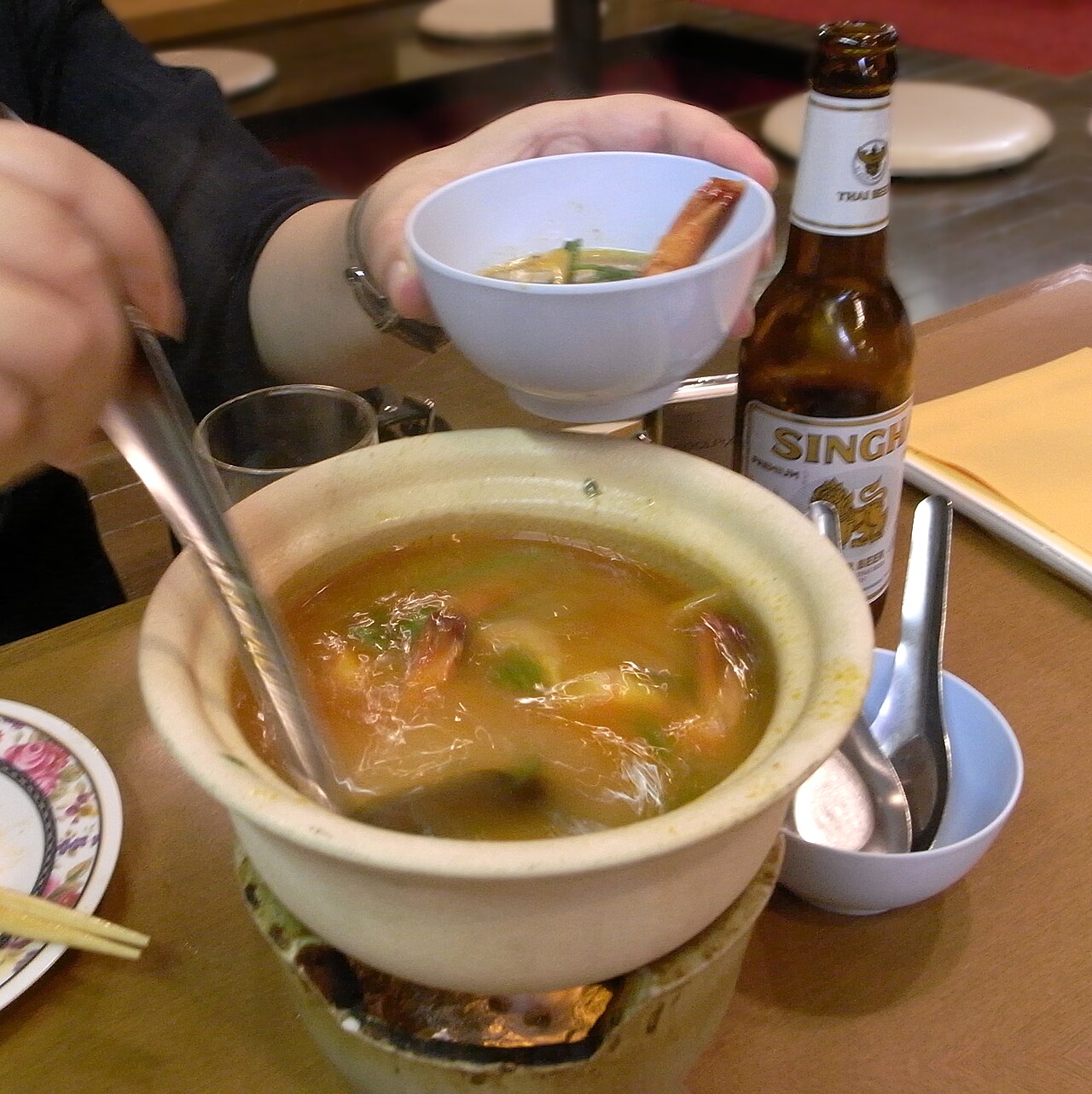 A steaming clay pot of tom yum goong, orange-red hot-and-sour broth with big sea prawns, lemongrass, galangal and kaffir lime