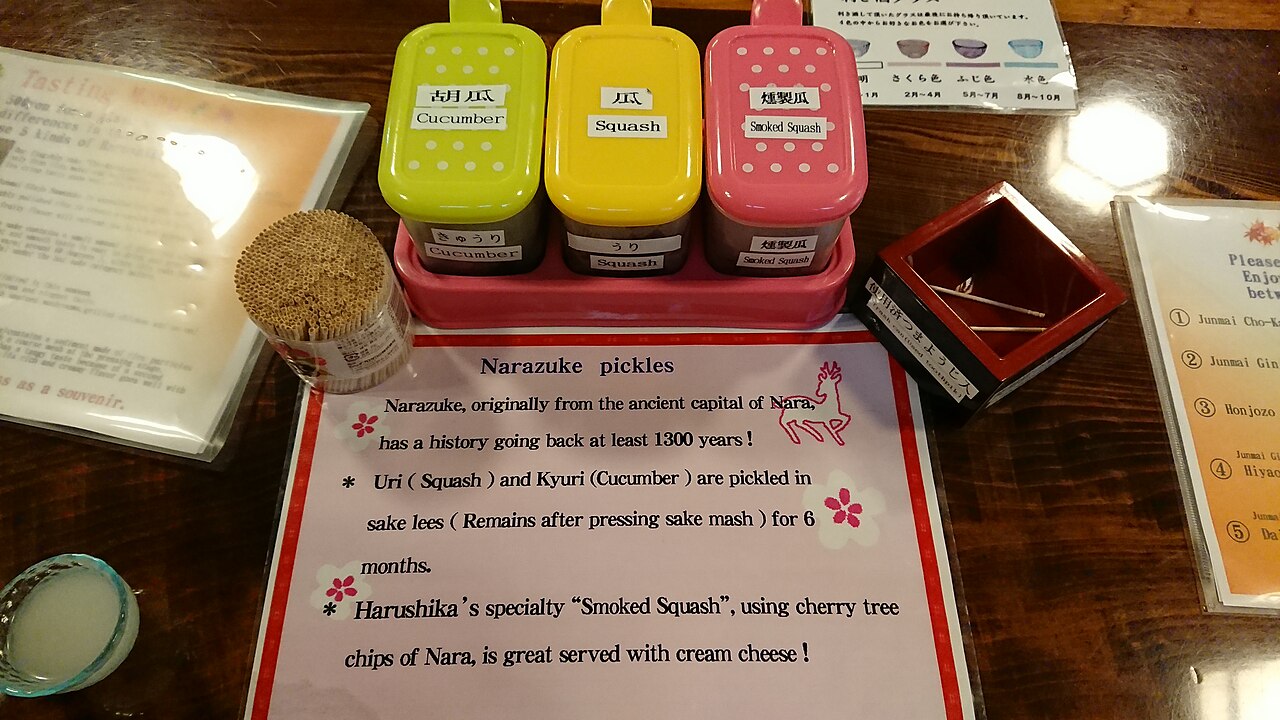 Narazuke sake-lees pickles from Nara: three labelled sample containers (cucumber, squash, smoked squash) in green, yellow, and pink lids at Harushika Sake Brewery, with an English explanation card in front