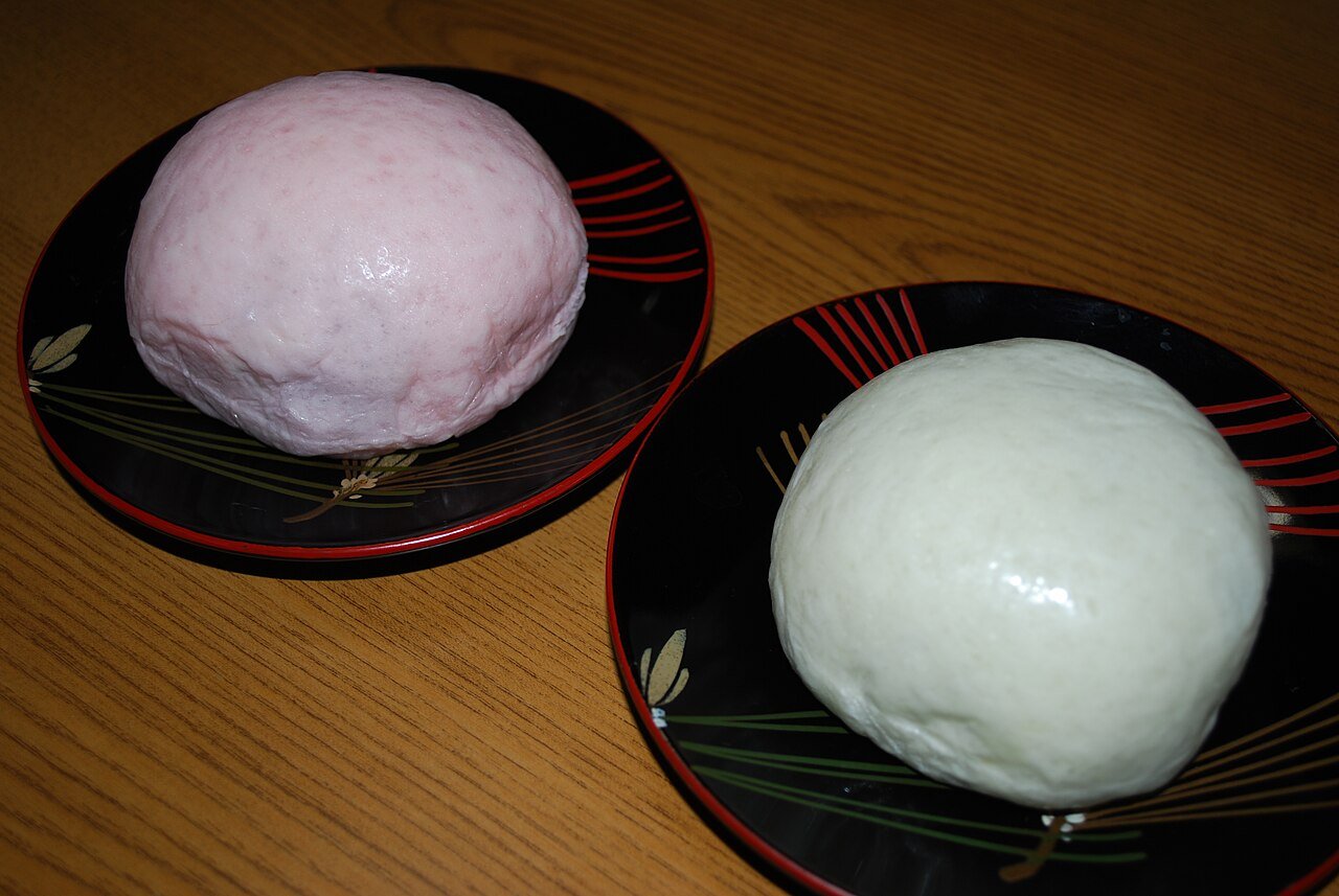 Nikko manju, two steamed buns — one pink and one white — resting on black lacquer plates with copper-coloured trim, a traditional sweet and souvenir