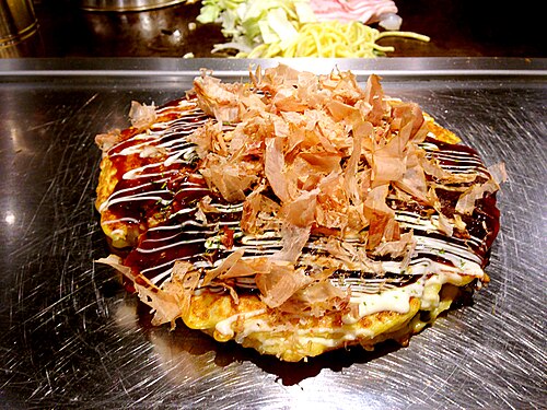Osaka-style okonomiyaki on a golden-brown iron griddle, topped with sauce, mayonnaise and bonito flakes